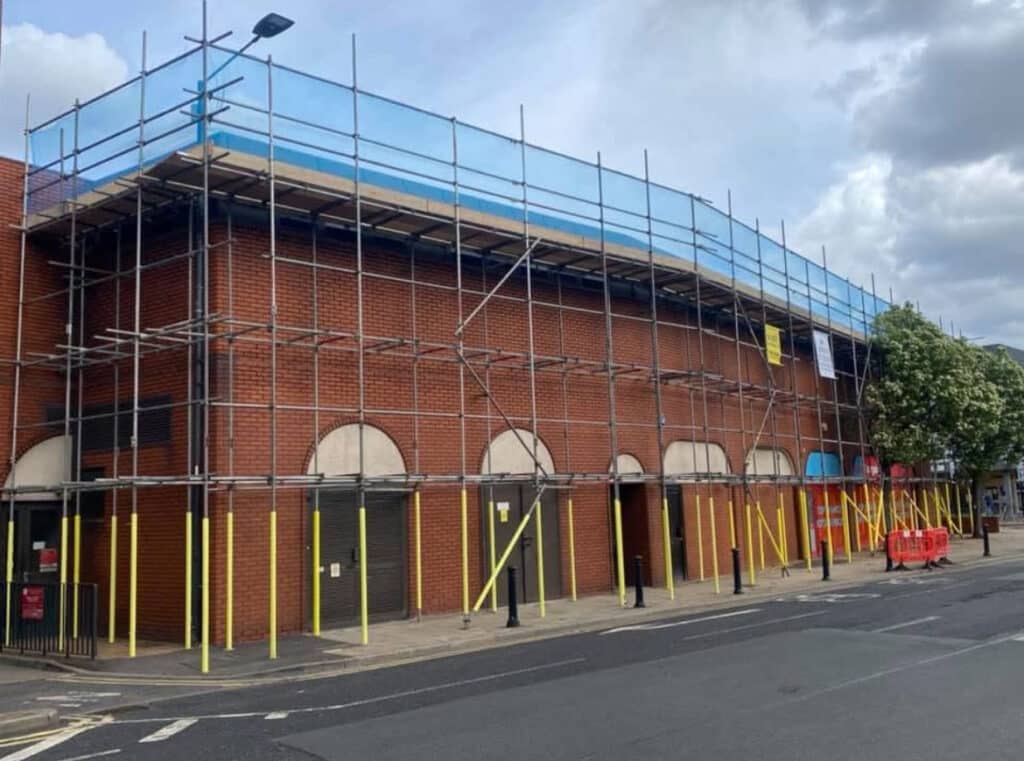 Large-scale UK building works: full facade scaffolding with blue debris netting, concrete walls