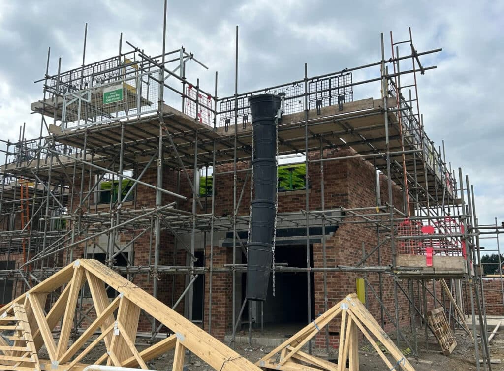 Scaffolding surrounding a new brick house under construction with large black chimney flue installed