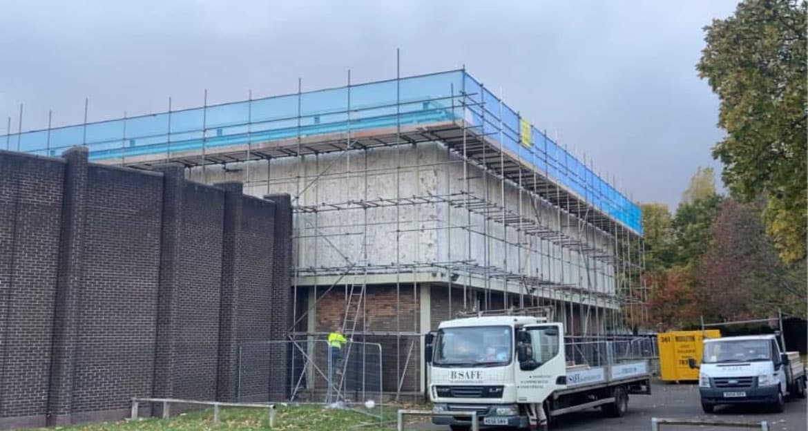 Extensive tube scaffolding with blue mesh enclosure on a multi-storey industrial structure during construction or refurbishment